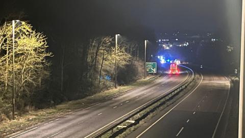 Emergency workers attend a crash on the A1 near Grantham. The image was taken at night so the sky is dark and the road is bathed in street light. Blue lights on the emergency vehicles are visible.