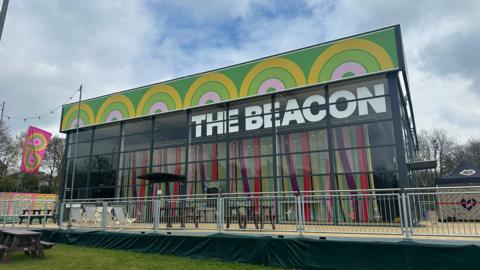 A glass and metal-framed building with the words The Beacon written in white letters on its side.