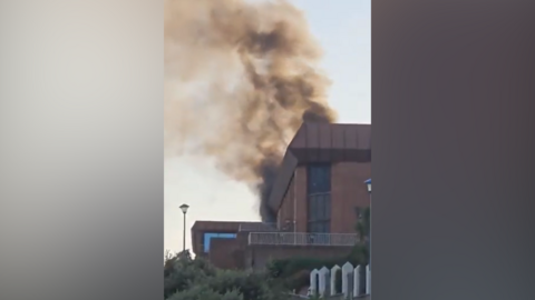 Smoke rising from the top of the red brick building with a distinctive brown flat roof