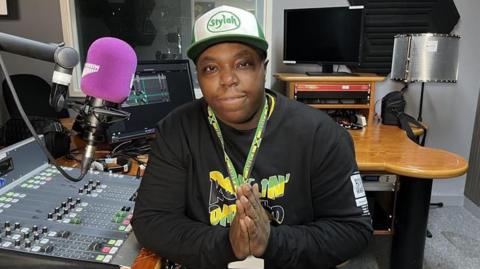 Tyrell-Jordan Blackwood sits in a radio studio at North Kent College in Dartford wearing a Jamaica flag designed sweatshirt and baseball cap that reads 'Stylah'