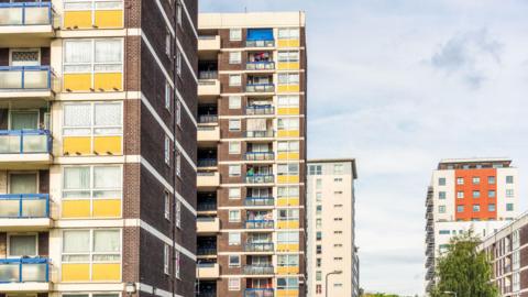 A side view of three older residential tower blocks in a row with a a new block to the right of the image. 