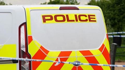 A generic picture of a white police van which has orange and yellow markings and a blue and white police tape in front of it.