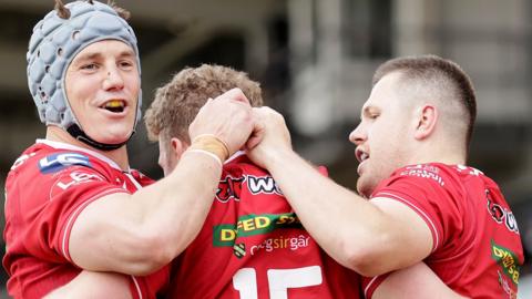 Jonathan Davies (L) and Rob Evans (R) help Angus O'Brien celebrate a Scarlets try