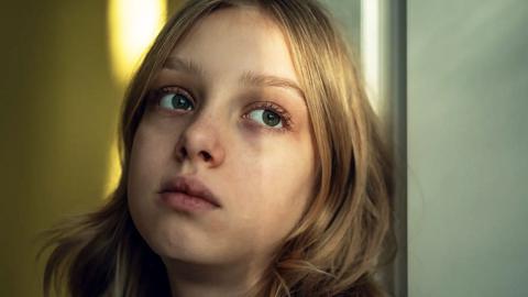 A girl with long blonde hair looking into the distance with a sad expression on her face