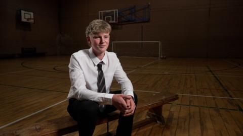 Sport student Loui sits on a wooden bench in the school sports hall