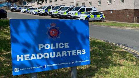 A large blue sign with Police Headquarters written on it. there are parked police cars in the background.
