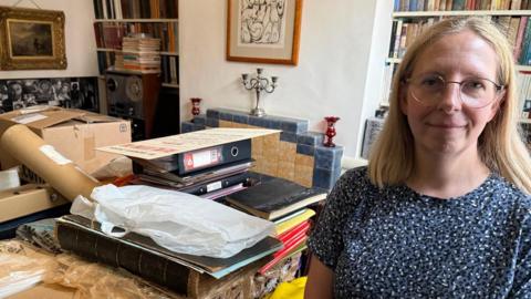 Elizabeth stands infront of the archive which is spread across her dining room table