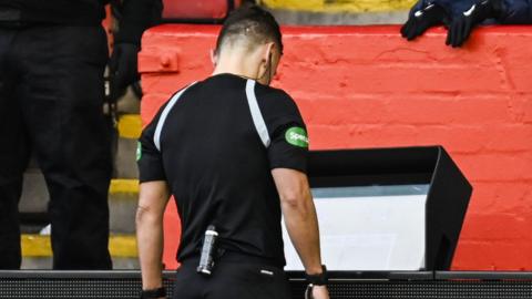 Referee Nick Walsh looks at the monitor during a VAR check