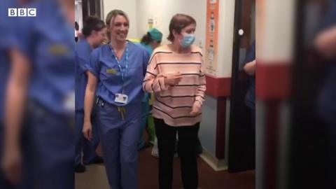 A nurse assisting a patient walking down a corridor