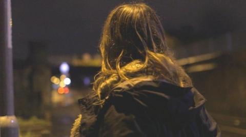 the back of a woman's head as she looks down a dark street.