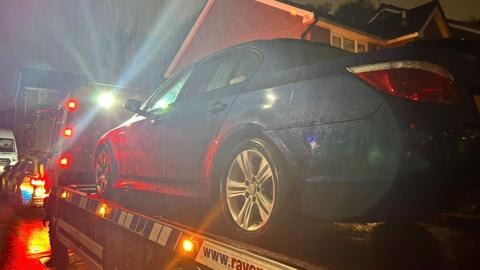 a blue BMW 520D on the back of a flatbed truck at night time.