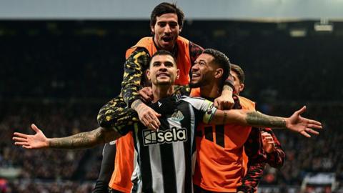 Bruno Guimaraes stands with his arms out celebrating, with Sandro Tonali and Joelinton with him
