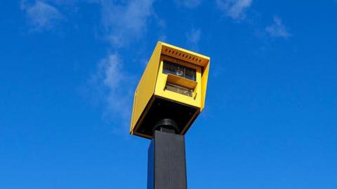 A yellow speed camera against a blue sky