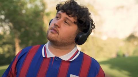 Partially-deaf singer James Vickery, a man with a short beard, wearing headphones and wearing a red and blue striped football shirt.