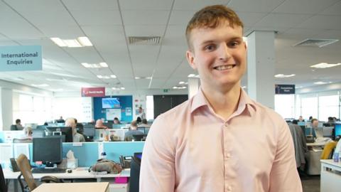 Man in office environment wearing pale pink t shirt. 