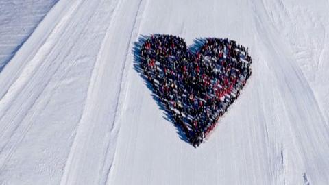 Skiers form the shape of a heart on a ski field from birds-eye-view