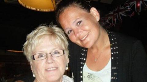 A woman with blonde hair and glasses pictured smiling next to her daughter, who is also smiling. The woman on the left is wearing a white top and on the right a black jacket with studded collar over a white t-shirt.