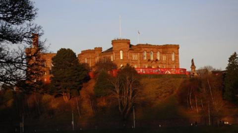 Looking up towards Inverness Castle which is lit in late evening sunlight.