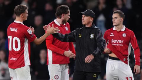 Gerhard Struber claps hands with Scott Twine (left) after full-time as Rob Dickie stands behind and Anis Mehmeti holds his hand under his shirt also behind him