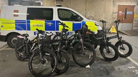 A police vehicle has a number of e-bikes propped up in front of it inside a garage
