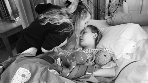 A woman next to her daughter who is receiving treatment at a hospital.