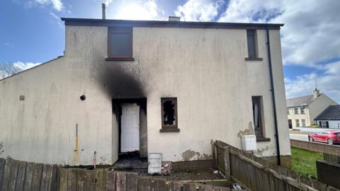 A white house with fire damaged windows and door