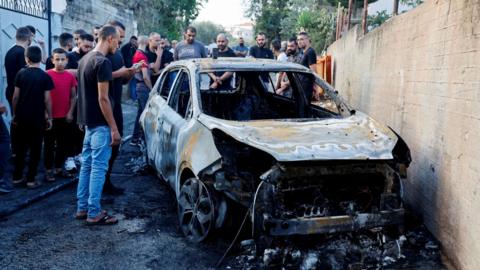 Palestinians inspect a burned-out car in Zababdeh, in the north of the occupied West Bank,  following an operation in which the Israeli military said a local Hamas commander and two other Palestinian fighters were killed (30 August 2024)