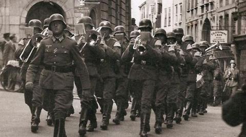 German soldiers in uniform, some playing musical instruments, march in front of the Lloyds bank building in St Peter Port 