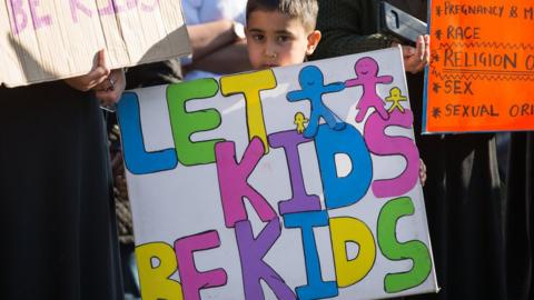 Child holding banner saying "Let kids be kids"