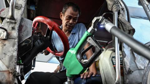 A driver looks down from within his car as he fills his jeep with diesel in Manila on 6 March