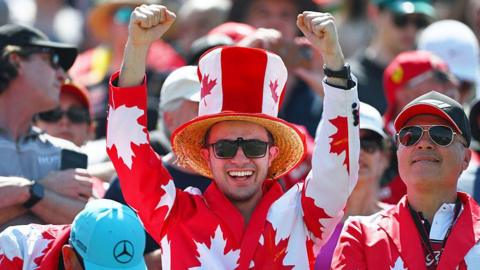 A fan in the grandstand waves his arms in the air while wearing a Canadian themed suit. 
