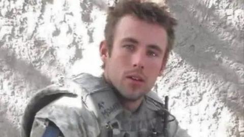 A head and shoulders shot of Sam Morgan wearing a uniform. He's a young man with short brown hair and is not smiling