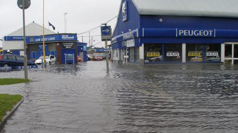 Flooding at West Quay Road, Poole, in 2008. A road sign saying "One Way" is in the middle of water. Two garages are in the background.