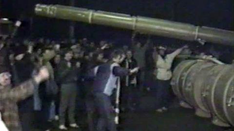 The barrel of a tank gun pointing over a crowd