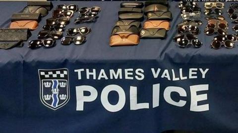 Sunglasses are displayed in rows on a table covered in a blue cloth which has the Thames Valley Police name and logo