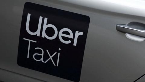 A close up picture of an Uber Taxi logo on a silver car. 