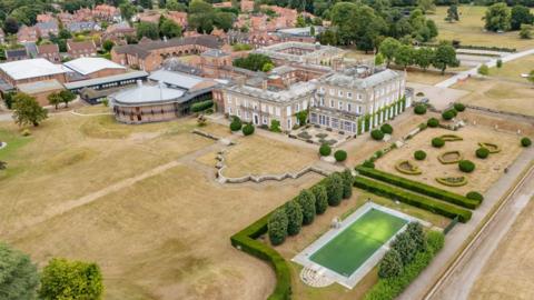 The property and grounds of Queen Margaret School for Girls'. A large historic building is surrounded by playing fields, manicured gardens and an outdoor swimming pool.