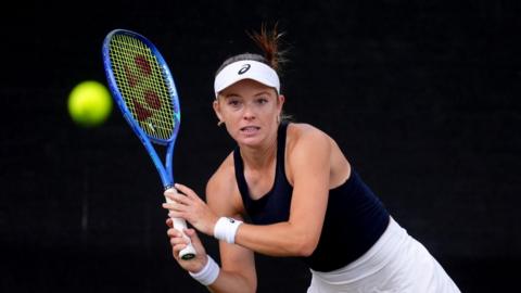 Katie Swan holding a tennis racket to her right as a ball flies towards her