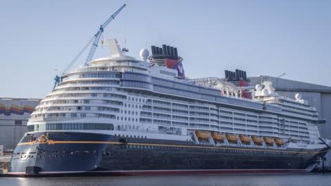 The Disney Treasure, a huge cruise ship, docked in a port. 