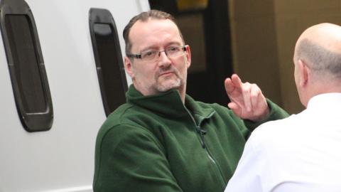 Alan Edward, wearing a green fleece top, is led from a custody van towards the court by an officer in a white shirt