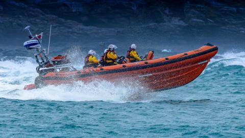 An Atlantic 85 inshore lifeboat - an orange RNLI boat with crew onboard heading out to sea.
