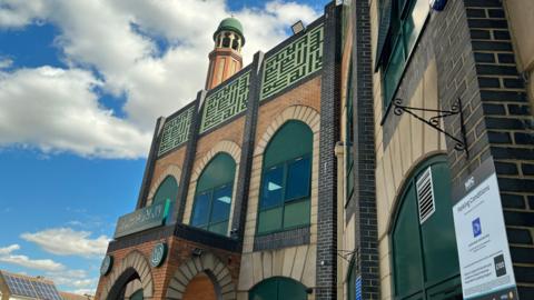 The facade of Faizan-e-Madina mosque including large green windows and an opening archway. 
