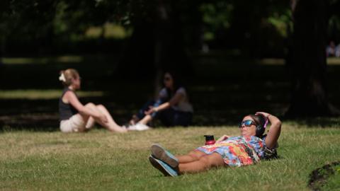 People lounging in the sun on the grass in St James Park in London 
