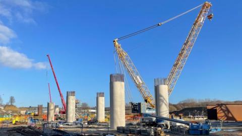 A large building site with a yellow crane towering above pillars that will form the base of a viaduct.