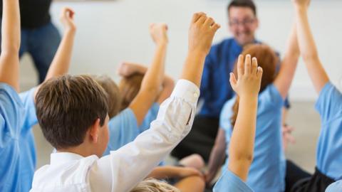 School children raising their hands in a classroom