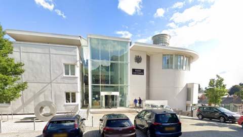 A picture of the front of Exeter Crown court. It is a white building with cars parked outside the front of it.
