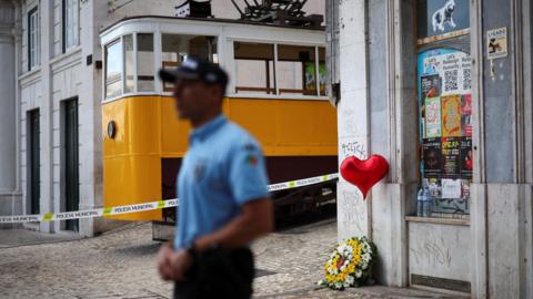  A wreath of flowers lies on the ground next to a balloon near the site of the accident