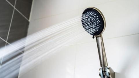 Water coming out of a silver-coloured shower head with white and black tiles behind