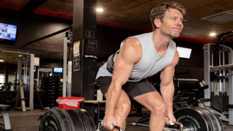 Dr Michael lifting weights at the gym in a grey singlet