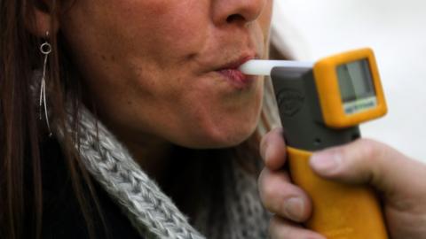 A stock image of a woman blowing into a breathalyser machine.